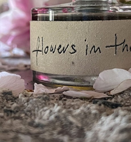Ilustracja dla zapachu Flowers in the ashes. Zbliżenie butelki perfum z żakardową etykietą stojącej w popiele.