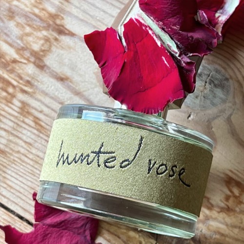 Ilustracja do perfum Hunted Rose. Zbliżenie leżącej niedbale butelki z odręcznym napisem.